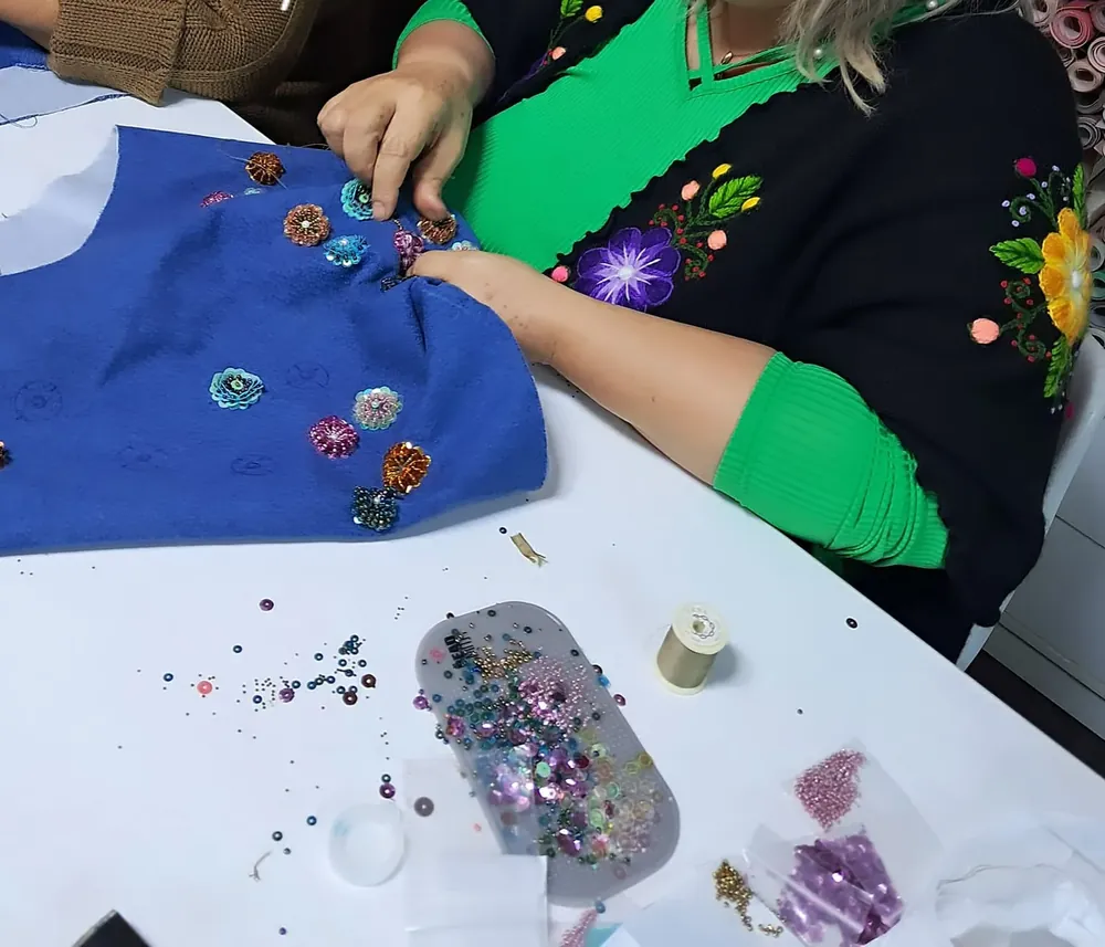 Alumna bordando apliques en pedrería sobre tela azul durante una clase