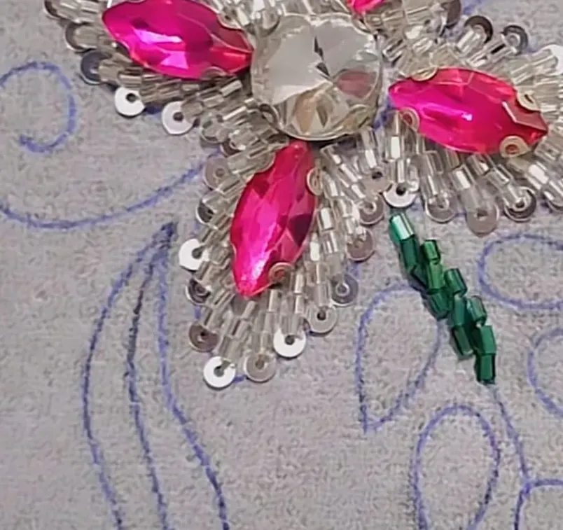 Flor de cristales fucsia con mostacilla y lentejuelas plateadas sobre un dibujo en tela
