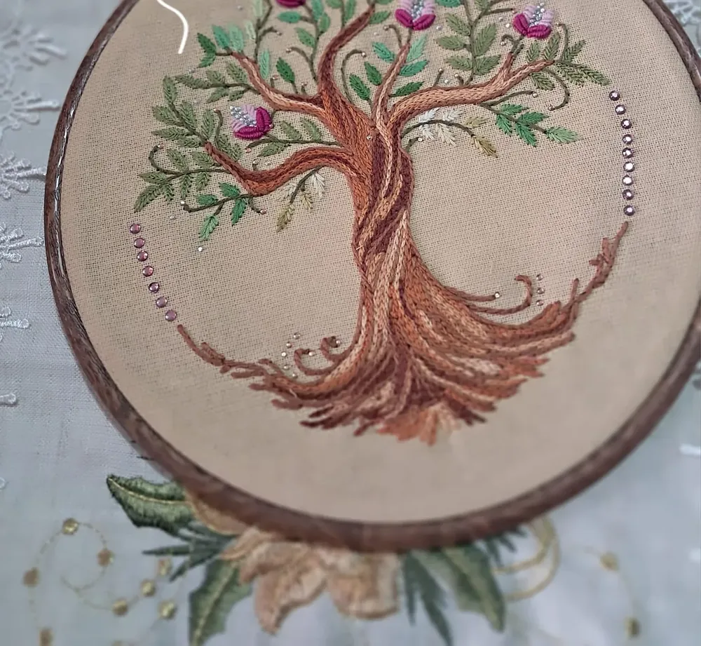 Árbol de la vida bordado en hilo marrón con flores rosadas, en bastidor de madera
