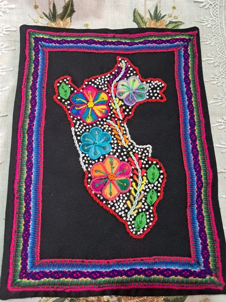 Mapa del Perú bordado con flores de colores y contorno de mostacilla, enmarcado en un tejido de franjas