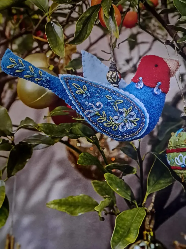Pajarito de fieltro azul bordado con hilos y mostacilla, colgado de un árbol