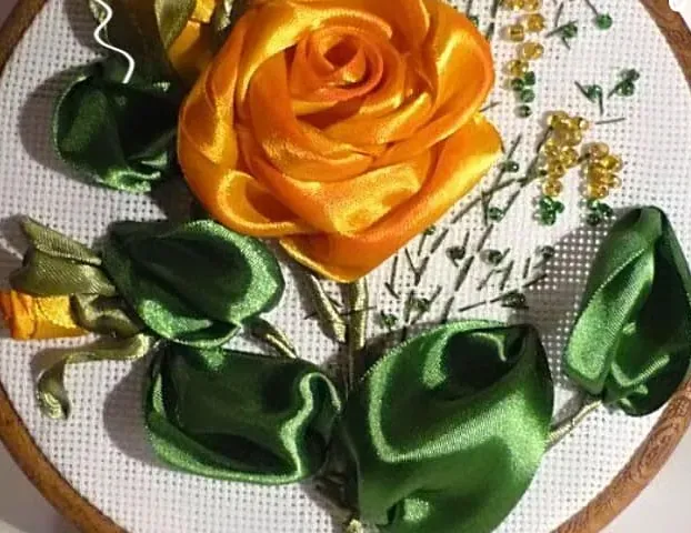 Rosa amarilla de cinta de raso con hojas verdes, en un bastidor