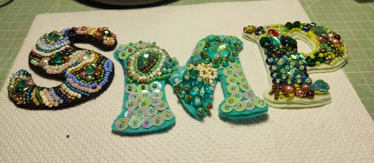 Letras bordadas en pedrería verde, turquesa y dorada