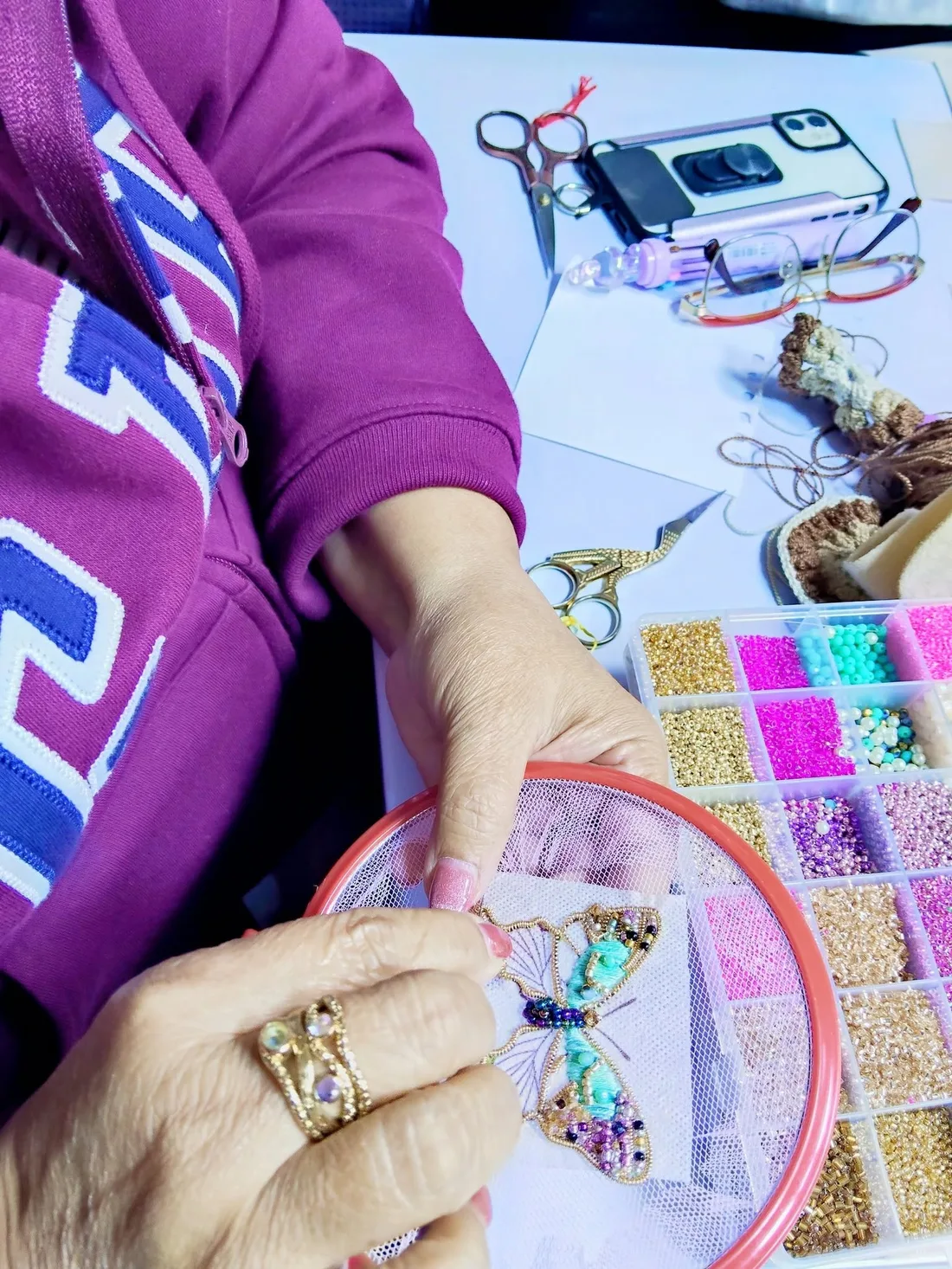 Bastidor con una mariposa en pedrería junto a una caja de mostacillas de colores